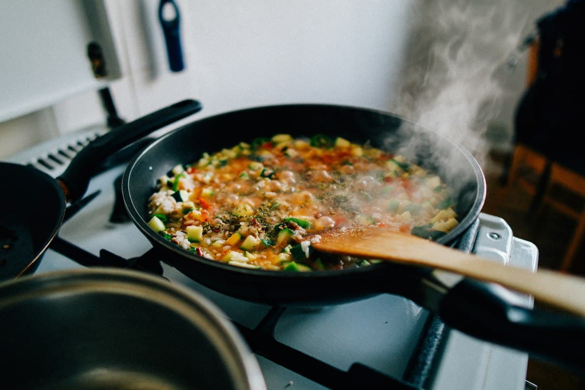 A pan of vegetables and rice simmering on the stove, with steam rising